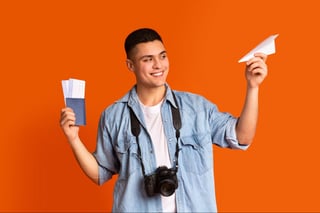 Playful guy traveler holding passport, flight tickets and paper airplane